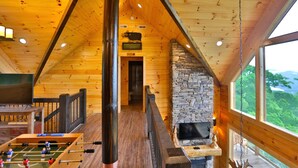 Un intérieur en bois avec une cheminée en pierre, un baby-foot et un téléviseur.