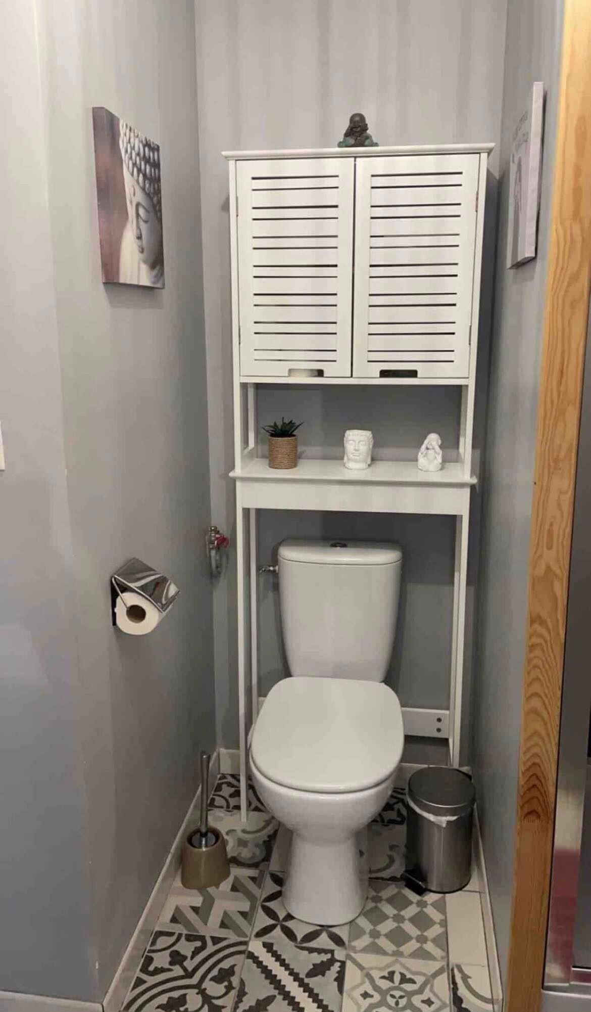 Een kleine badkamer met toilet, een klein plankje met decoratieve spullen en een vloer met patroon.