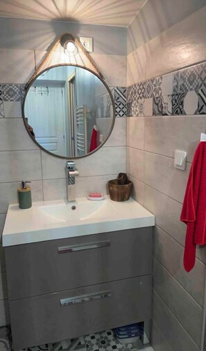 Une salle de bain avec un miroir rond, un lavabo, un porte-serviettes et un meuble de rangement.