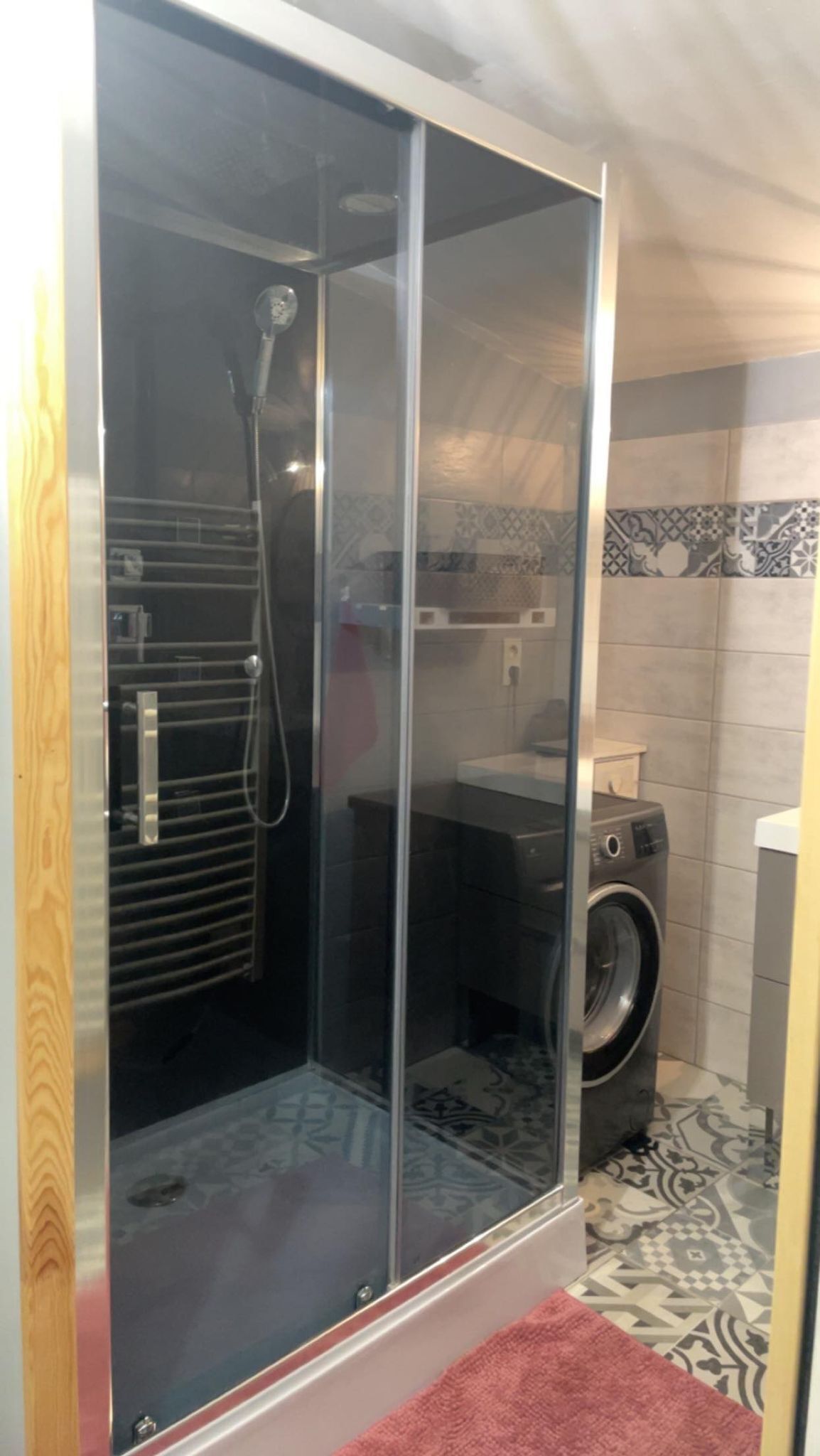 A shower enclosure with a glass door, a washing machine, and patterned tiles in the background.