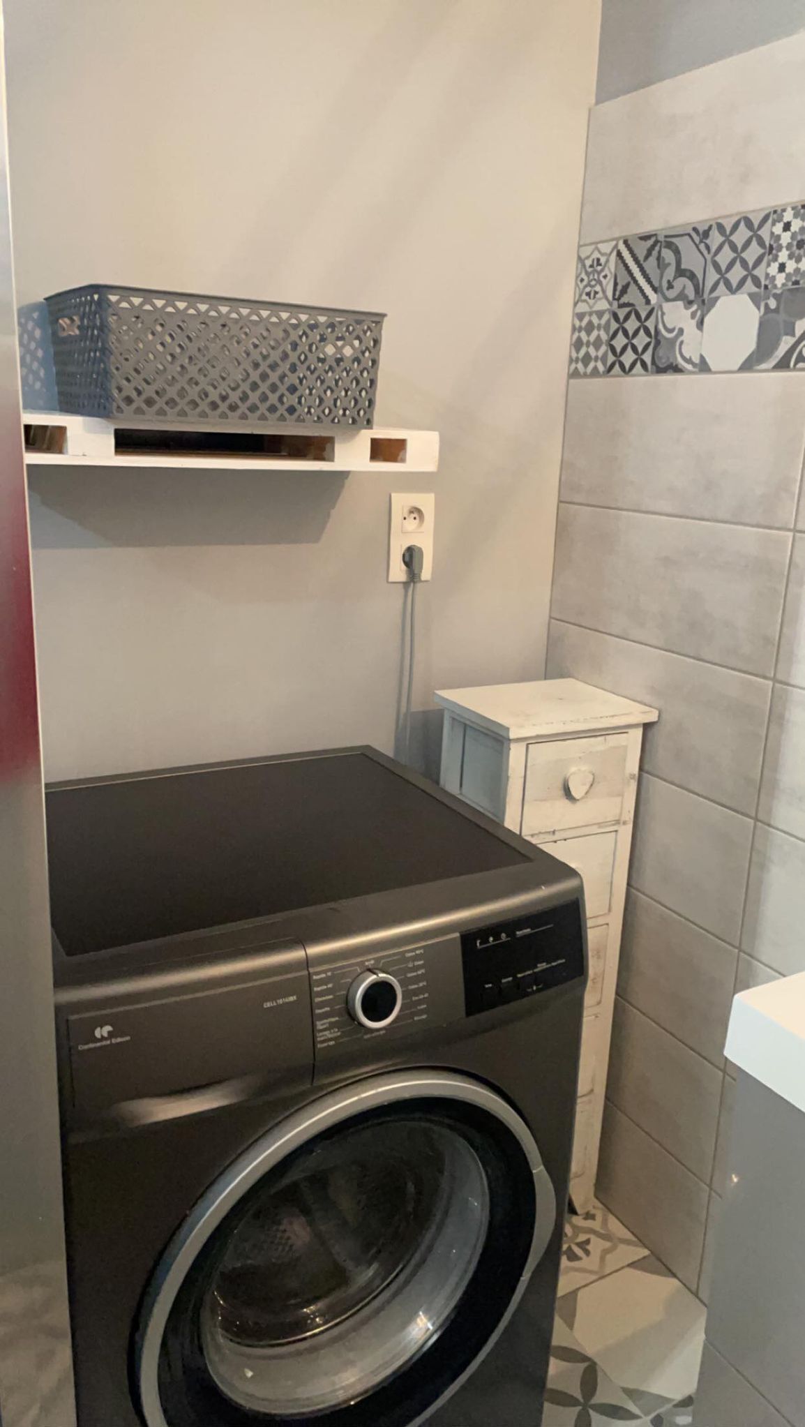 Un lavadero pequeño con lavadora de carga frontal, un armario blanco y una repisa con una cesta.