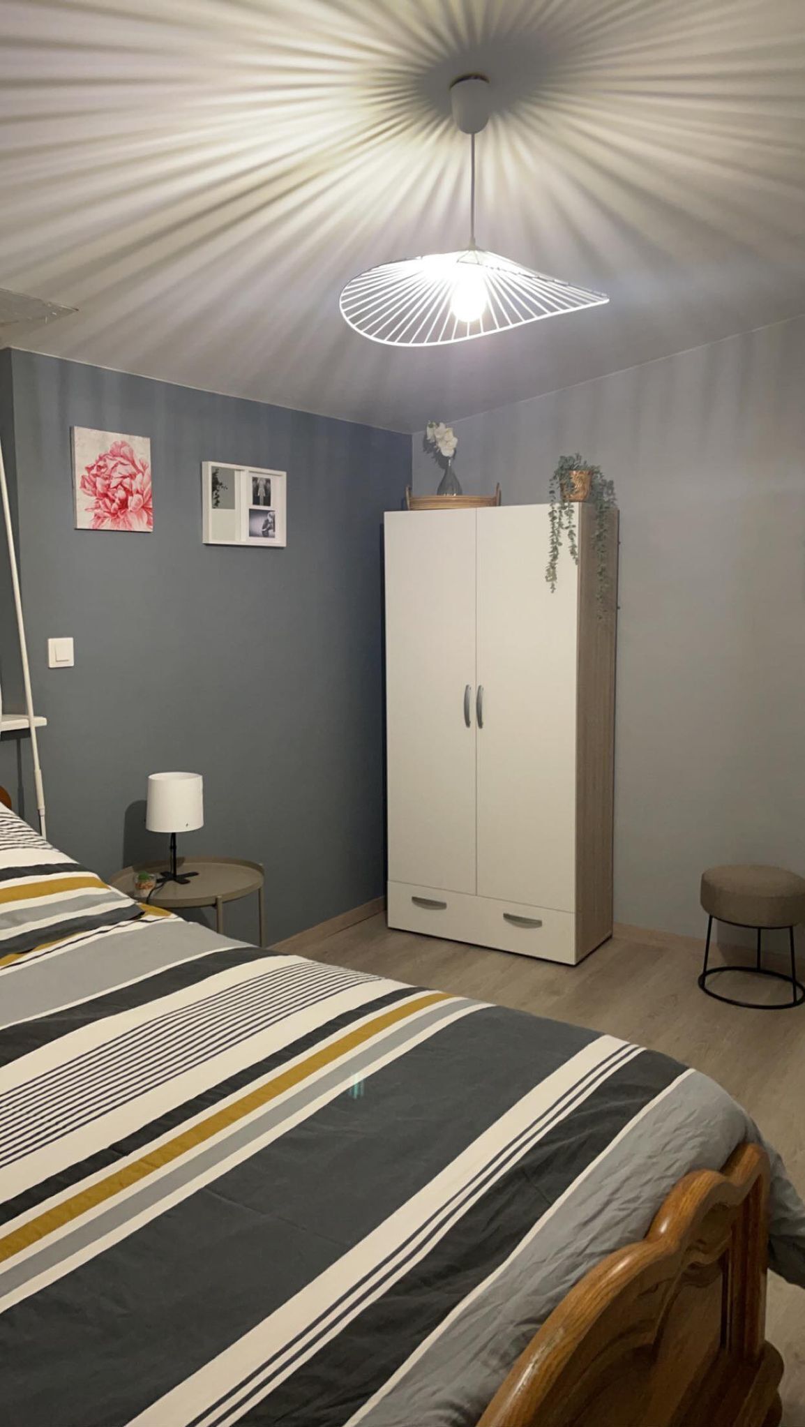 A bedroom with a bed, a wardrobe, a bedside table, a lamp, and a ceiling light fixture.