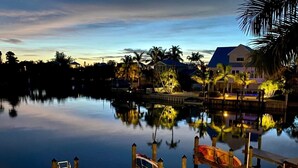 Una zona tranquila frente al agua con un muelle, barcos y casas con ventanas iluminadas.