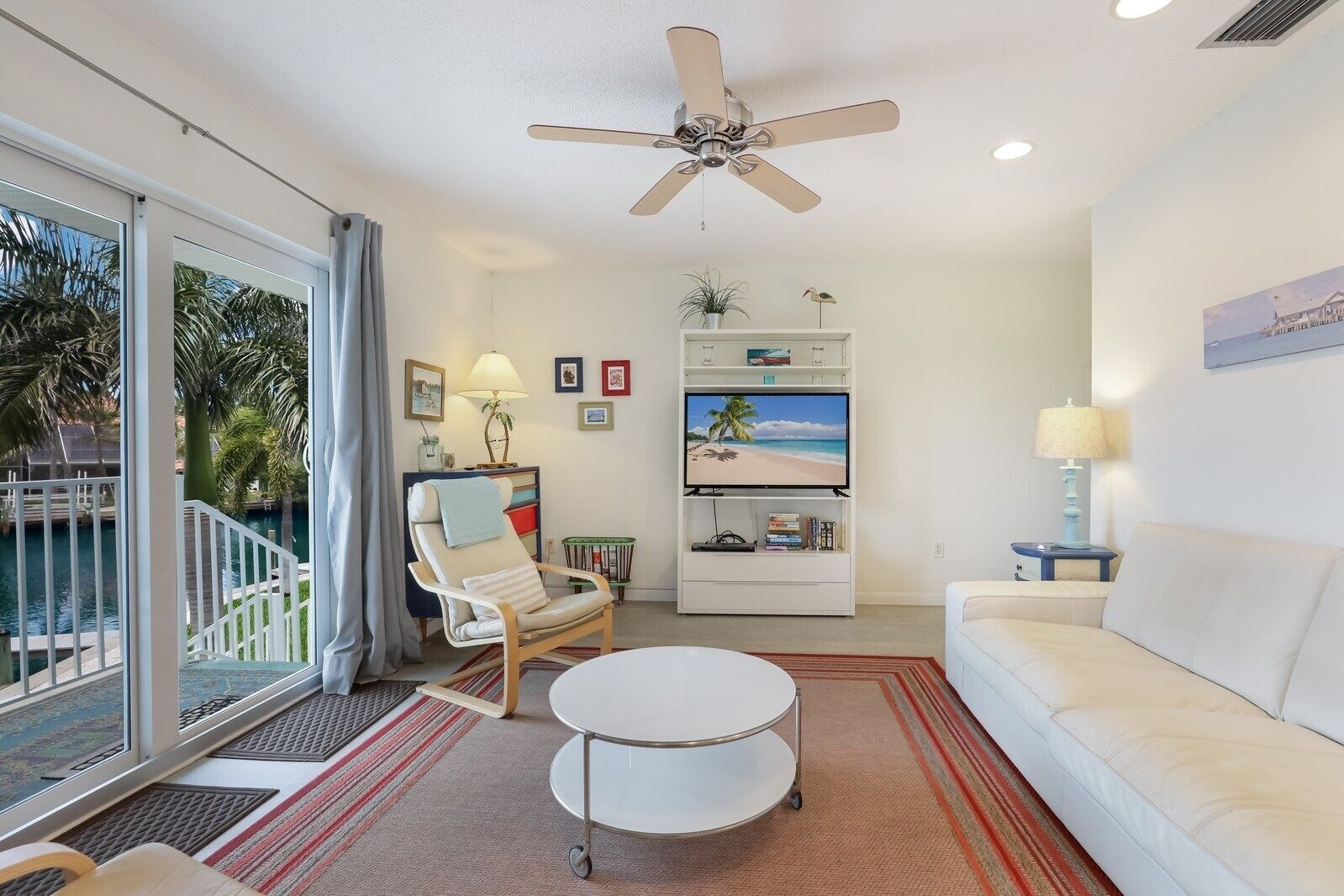 A modern living room with a ceiling fan, a TV on a stand, a white sofa, a chair, and a small table.