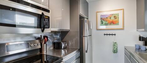 Une cuisine moderne équipée d’appareils électroménagers en acier inoxydable, d’un four à micro-ondes, d’un grille-pain et d’un réfrigérateur. Un tableau encadré orne le mur, et un sac est suspendu.
