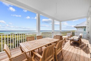 En træterrasse med et bord og stole, med udsigt over en strand og hav.