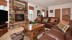 A living room with a stone fireplace, leather sofa, and a flat-screen TV. - Seven Springs 4 BR Premium Condo, Mountain Views! by RedAwning (Champion)