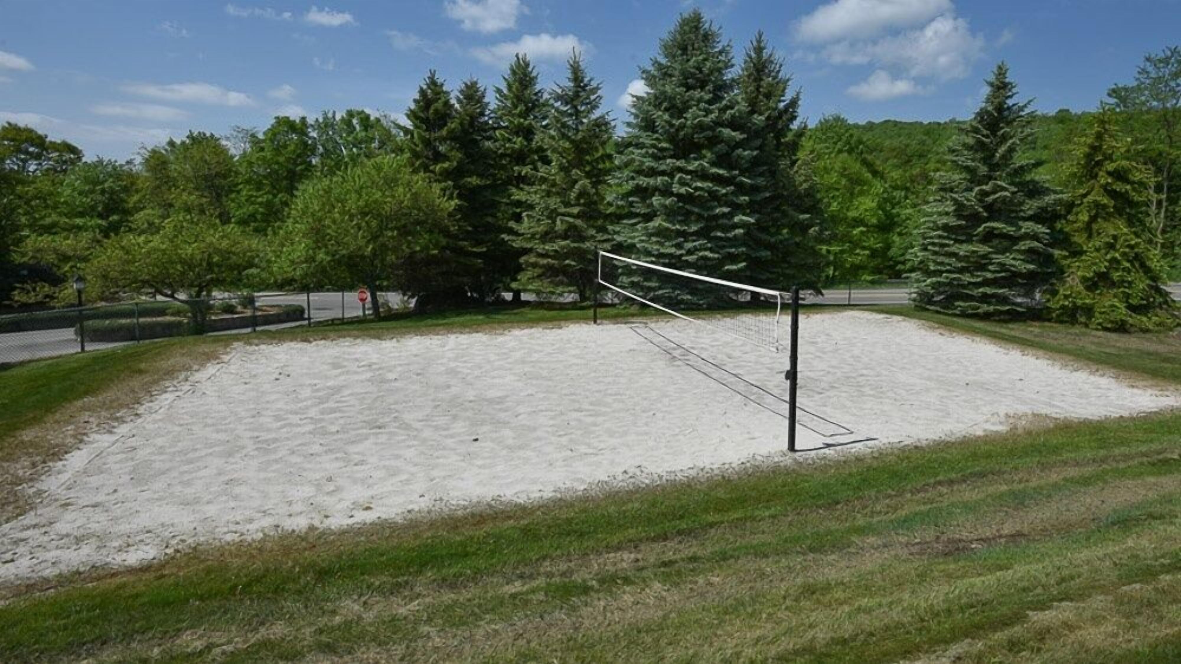 Ein Volleyballfeld mit Netz, umgeben von Sand und Gras, mit Bäumen im Hintergrund.