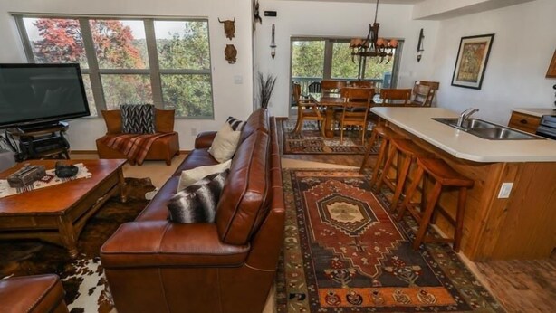 A spacious living room with a brown leather sofa, a television, and a dining area with a wooden table and chairs. - Seven Springs 4 BR Premium Condo, Mountain Views! by RedAwning (Champion)