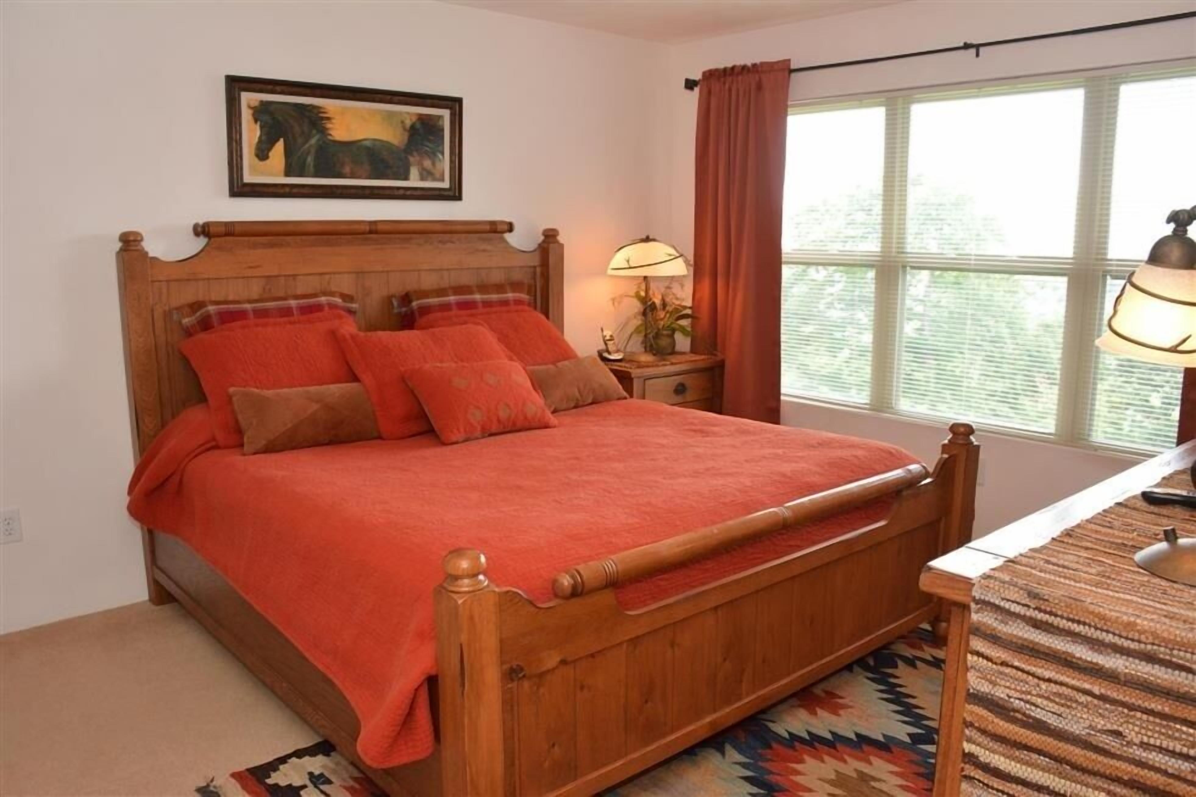 A wooden bed with a red blanket, a nightstand with a lamp, and a window with curtains.