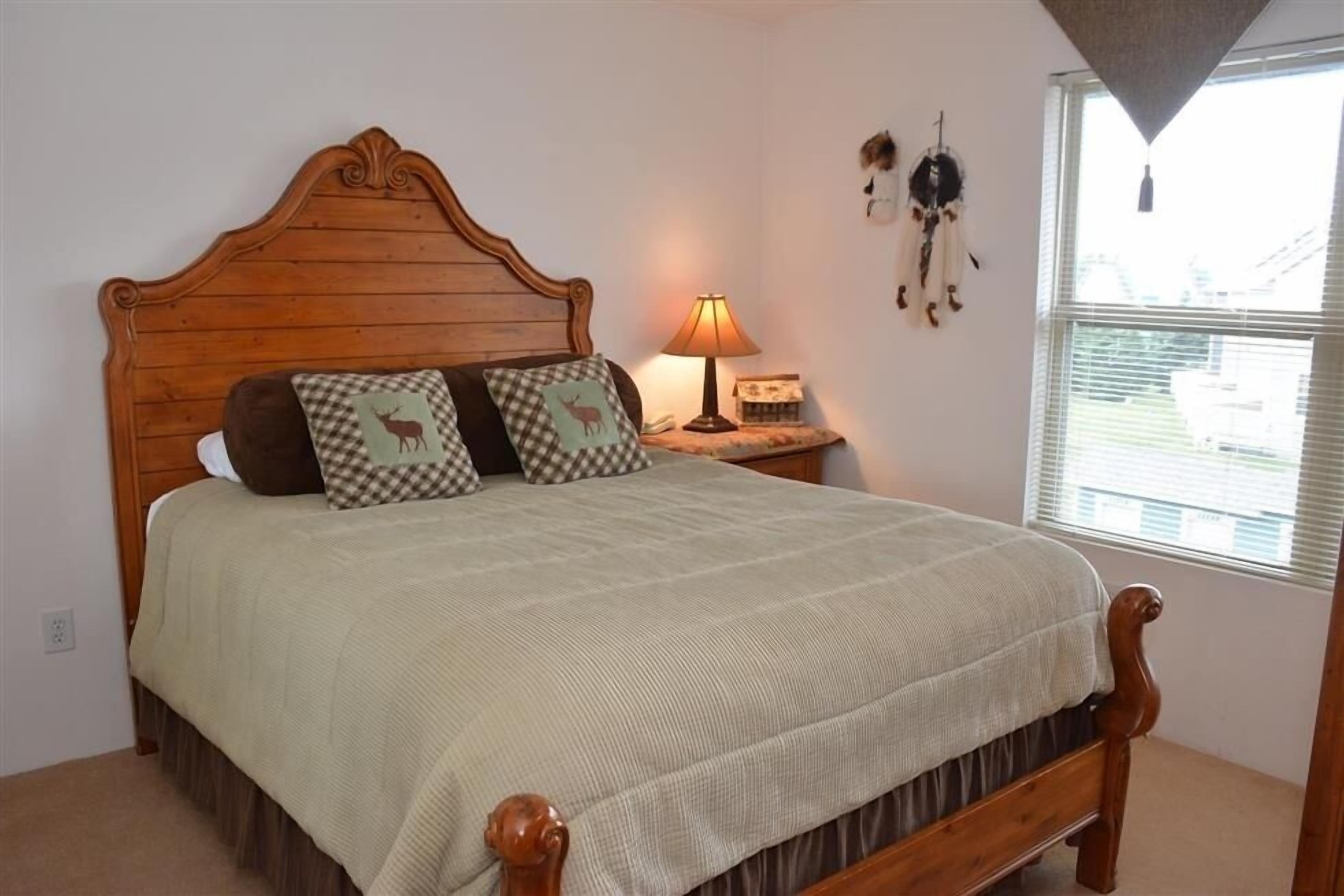 A bed with a wooden headboard, two pillows with a checkered pattern, a bedside lamp, and a wall with a dreamcatcher.