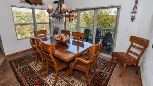 A dining area with a wooden table and chairs, a chandelier, and a view through large windows. - Seven Springs 4 BR Premium Condo, Mountain Views! by RedAwning (Champion)