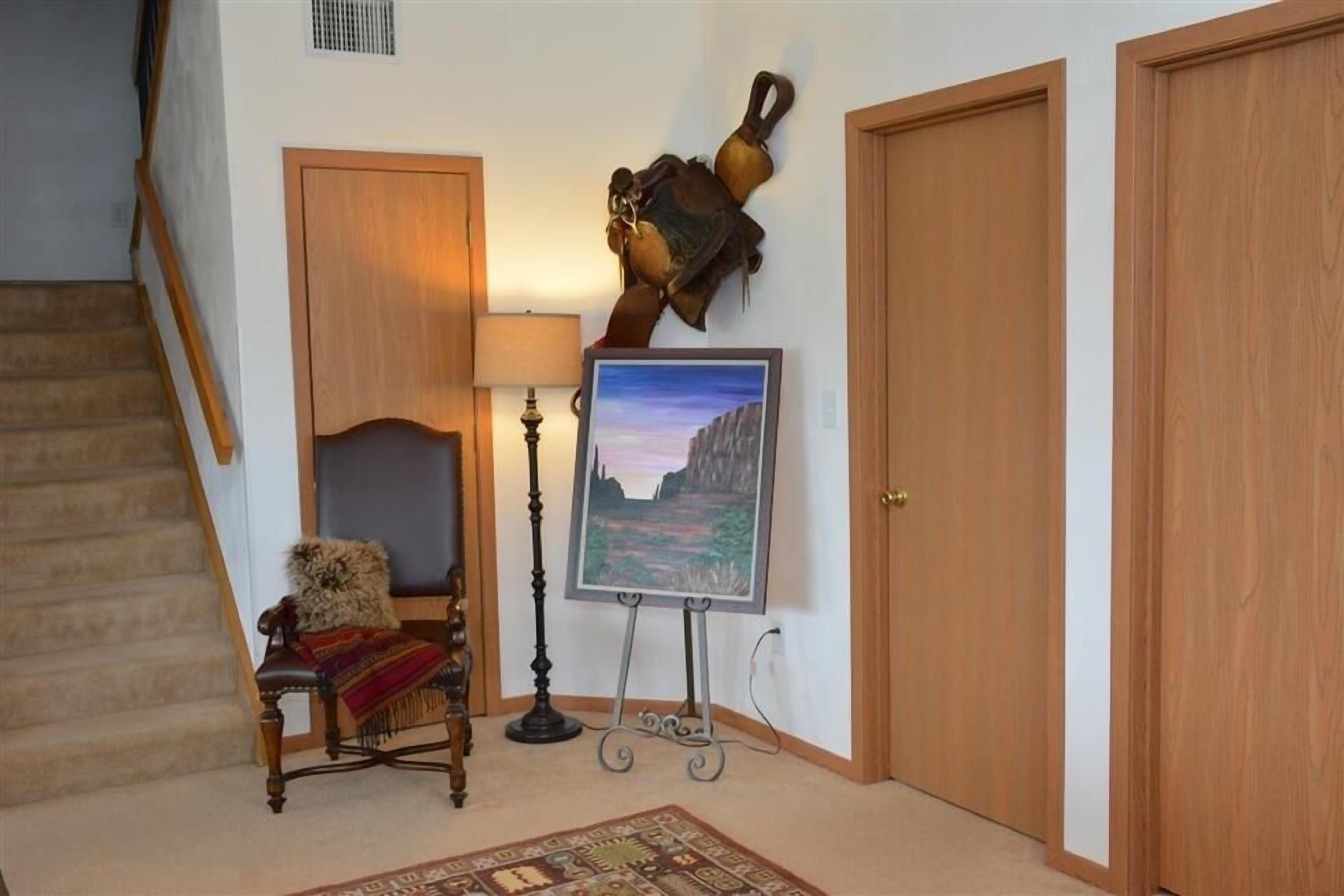 Un escalier menant à un palier où se trouve une porte en bois, un tableau encadré posé sur un chevalet, une lampe et une chaise recouverte d’une couverture.