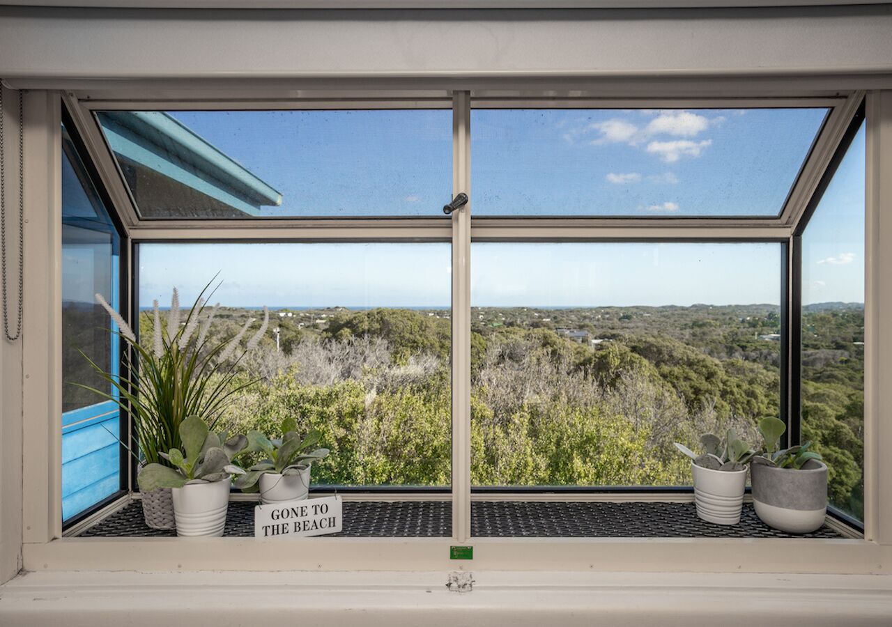 A window with a view of a landscape, a sign that says "GONE TO THE BEACH", and several potted plants on the windowsill.
