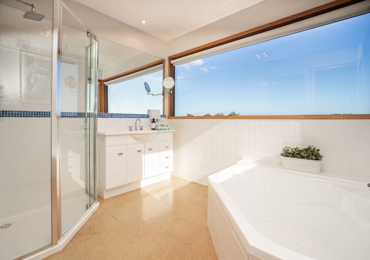 Een moderne badkamer met een glazen douchecabine, een ruim bad en een raam met uitzicht op de lucht.