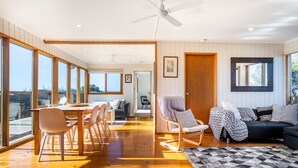 A spacious living room with a wooden floor, a dining area with chairs, a sofa, and a ceiling fan. - Moonah Horizon (Rye)