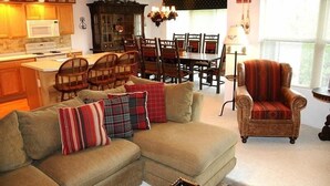A living room with a sectional sofa, a dining area with wooden chairs, a kitchen with a microwave, and a fireplace. - Seven Springs 4 BR Premium Condo, Deck with Views by RedAwning (Champion)