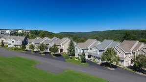 A row of modern, single-story houses with attached garages, set in a green, hilly area with a clear sky. - Seven Springs 4 BR Premium Condo, Deck with Views by RedAwning (Champion)