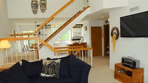 A living room with a dark-colored sofa, a wooden coffee table, a TV on a wooden stand, and a staircase leading to another room. - Seven Springs 2 BR Deluxe Condo, Mountain Views! by RedAwning (Champion)