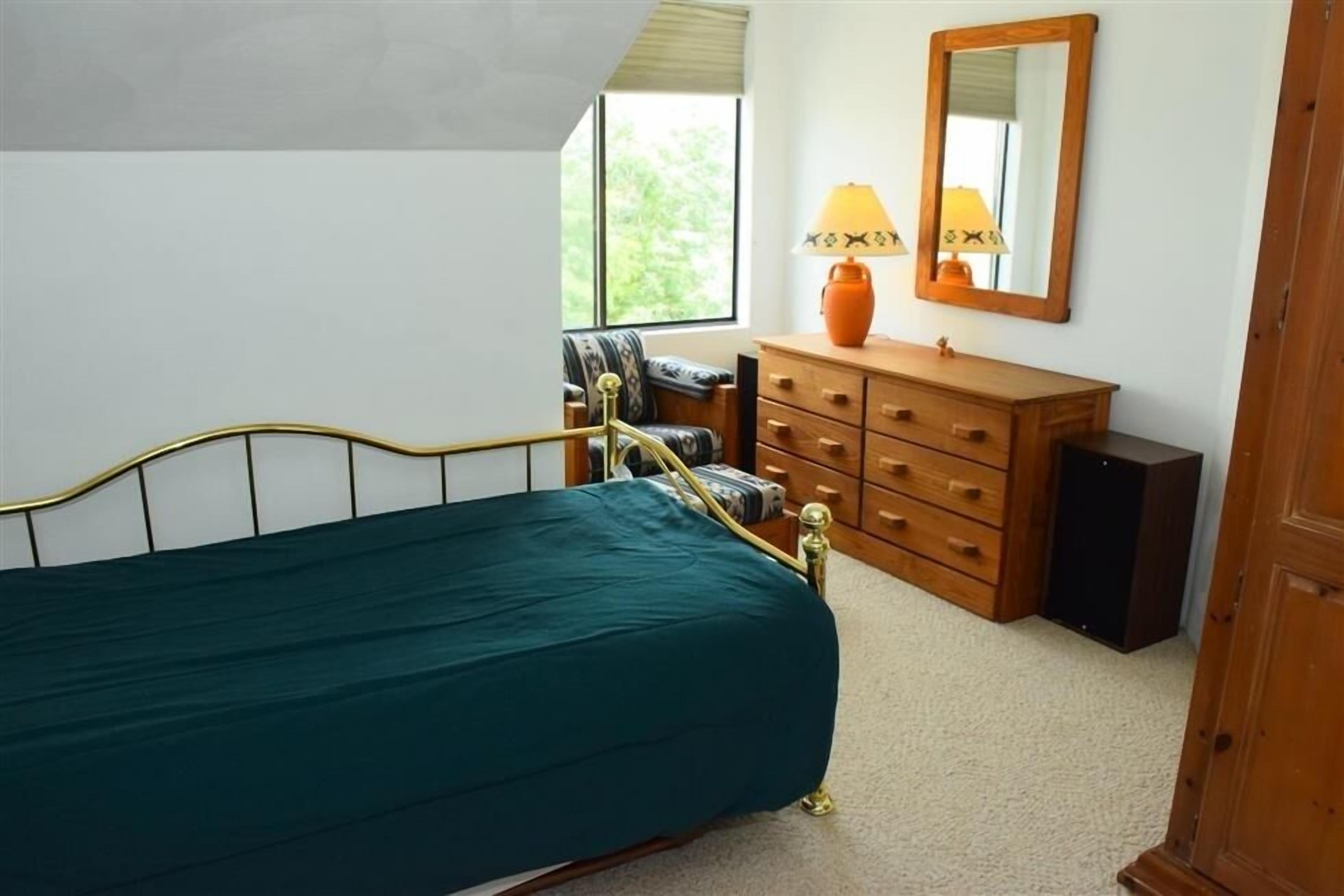 Quarto com cama, cômoda, cadeira, luminária e espelho.
