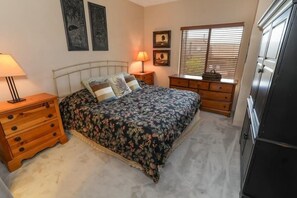 Une chambre à coucher avec un lit, des tables de chevet en bois, une commode et une fenêtre avec des stores.