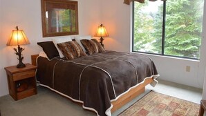 A bedroom with a large bed, two bedside lamps, a window with a view of trees, and a framed picture on the wall. - Seven Springs Sunridge 1 BR Loft Deluxe Condo, Ski-In/Out by RedAwning (Champion)