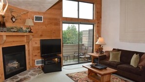 A cozy living room with a fireplace, a television, a sofa, and a dining table. - Seven Springs Sunridge 1 BR Loft Deluxe Condo, Ski-In/Out by RedAwning (Champion)