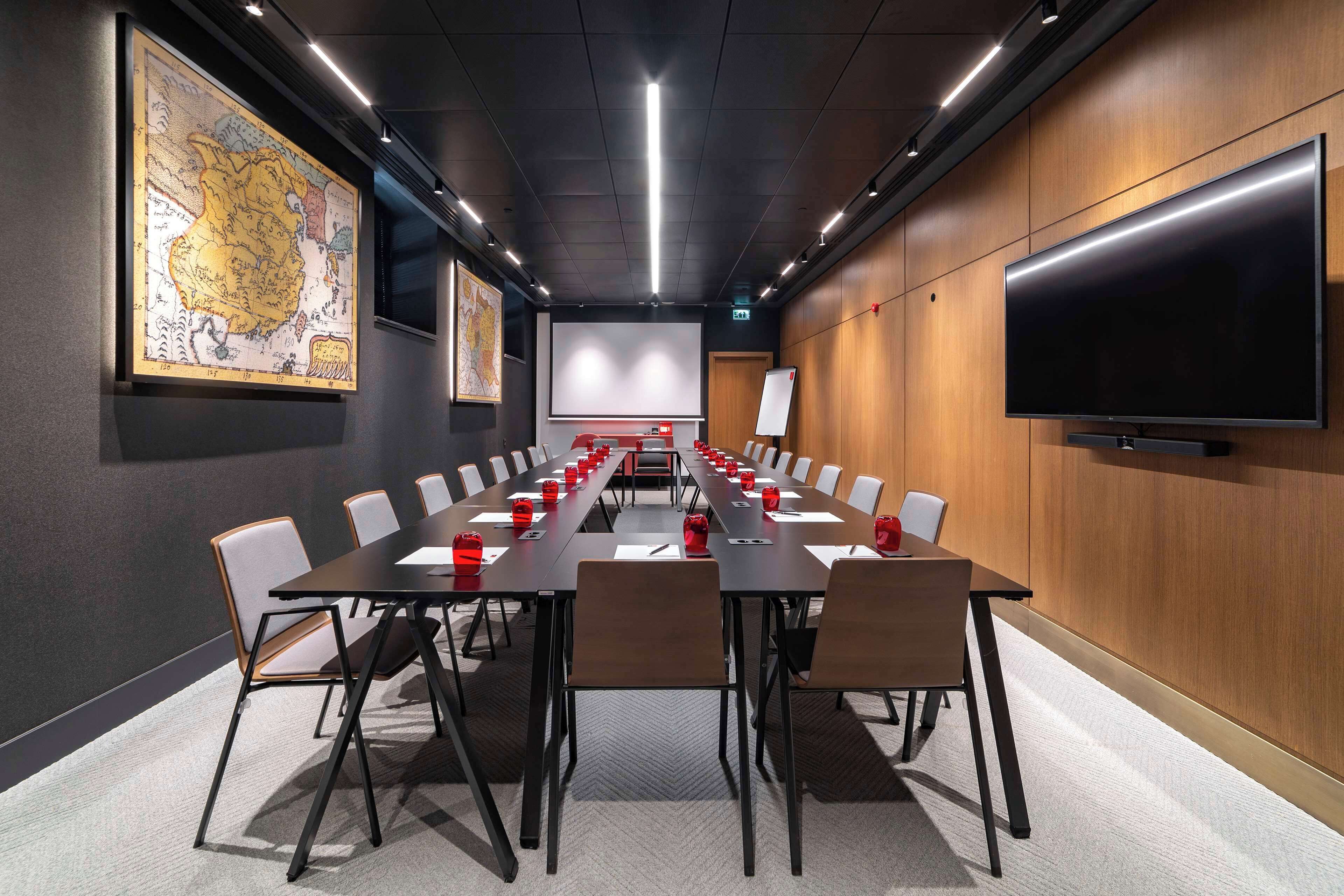 A conference room with a long table, chairs, a projector screen, and a large flat-screen TV.