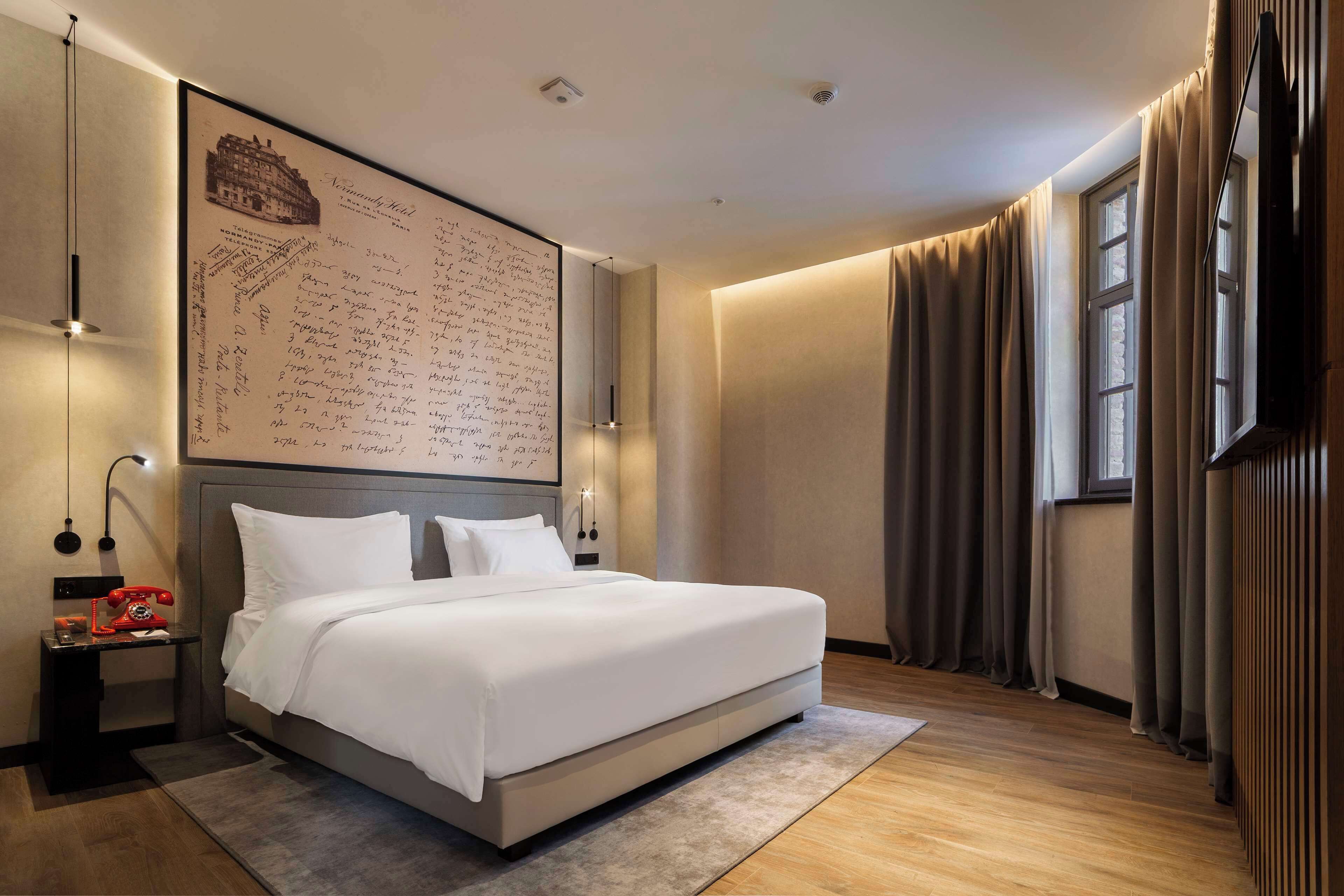 Een moderne hotelkamer met een groot bed, een nachtkastje met telefoon, een wandtelevisie en een grote ingelijste kaart.