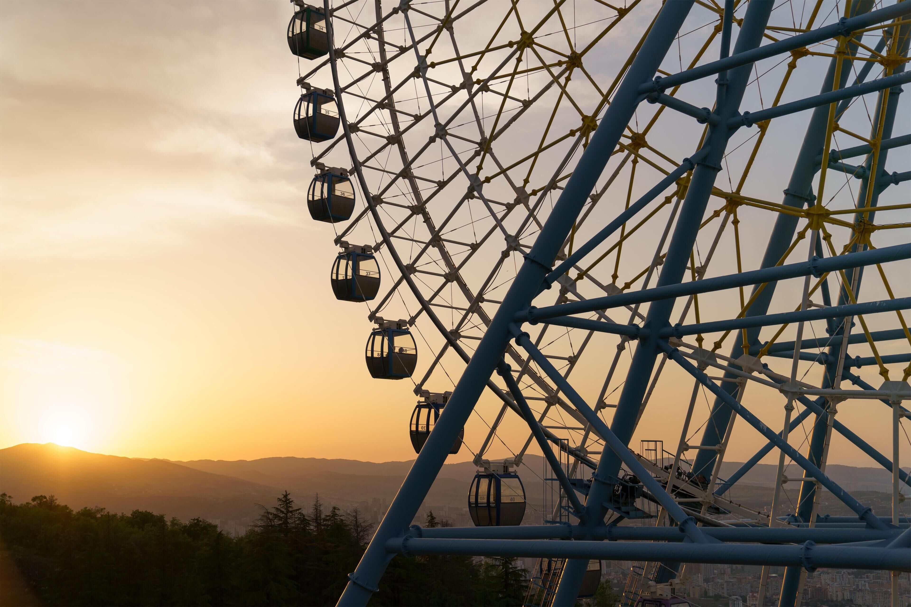 A Ferris wheel with gondolas, set against a sunset sky.