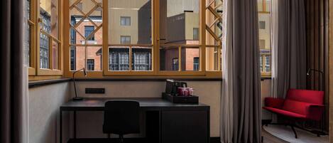 A modern room with a desk, chair, and a red sofa. A large window with curtains is visible, offering a view of buildings outside.