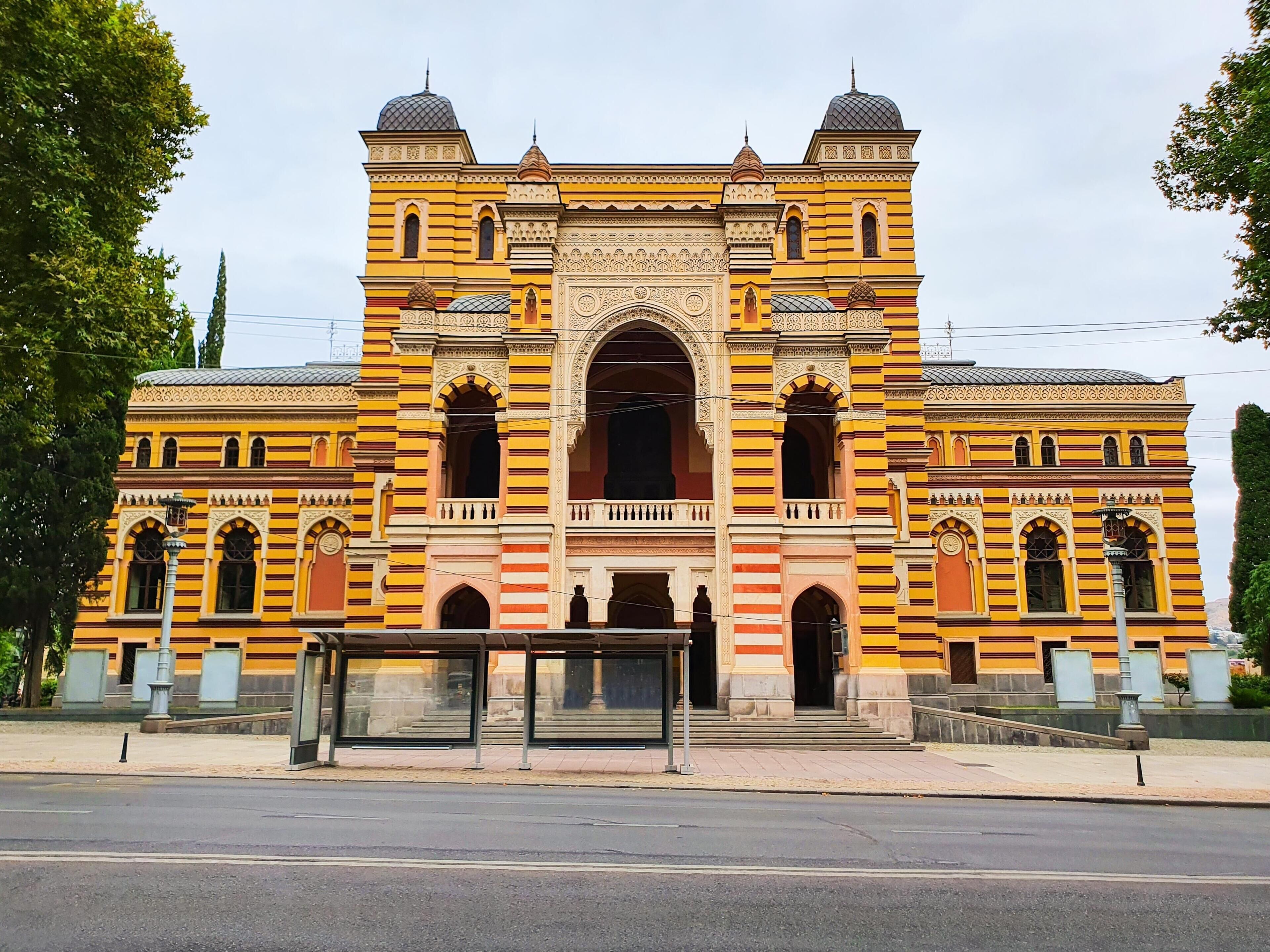 Ein großes, gelbes Gebäude mit einem zentralen Bogen und symmetrischer Gestaltung.