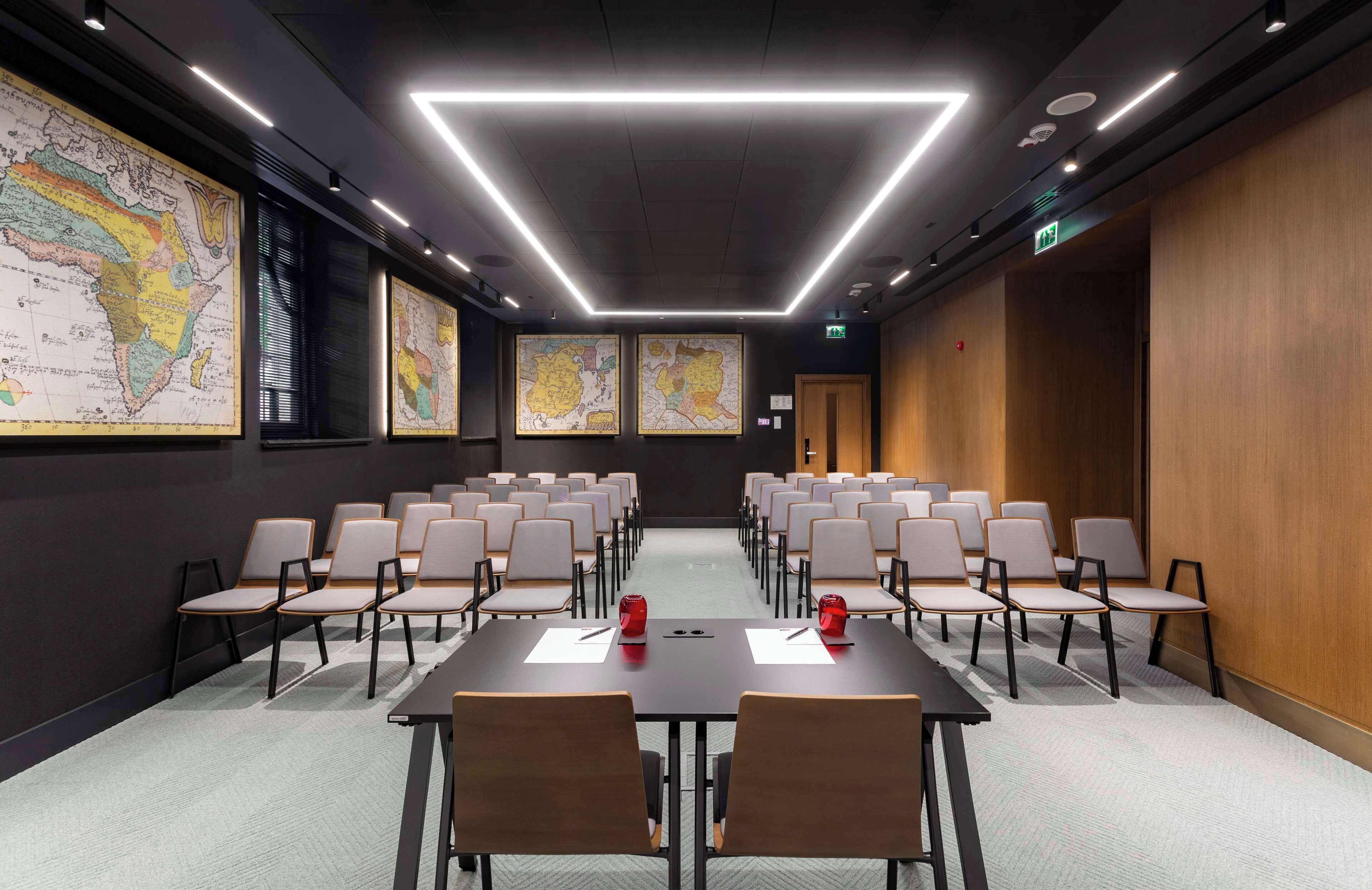 Un salón de conferencias con una larga mesa, varias sillas y grandes mapas en las paredes.