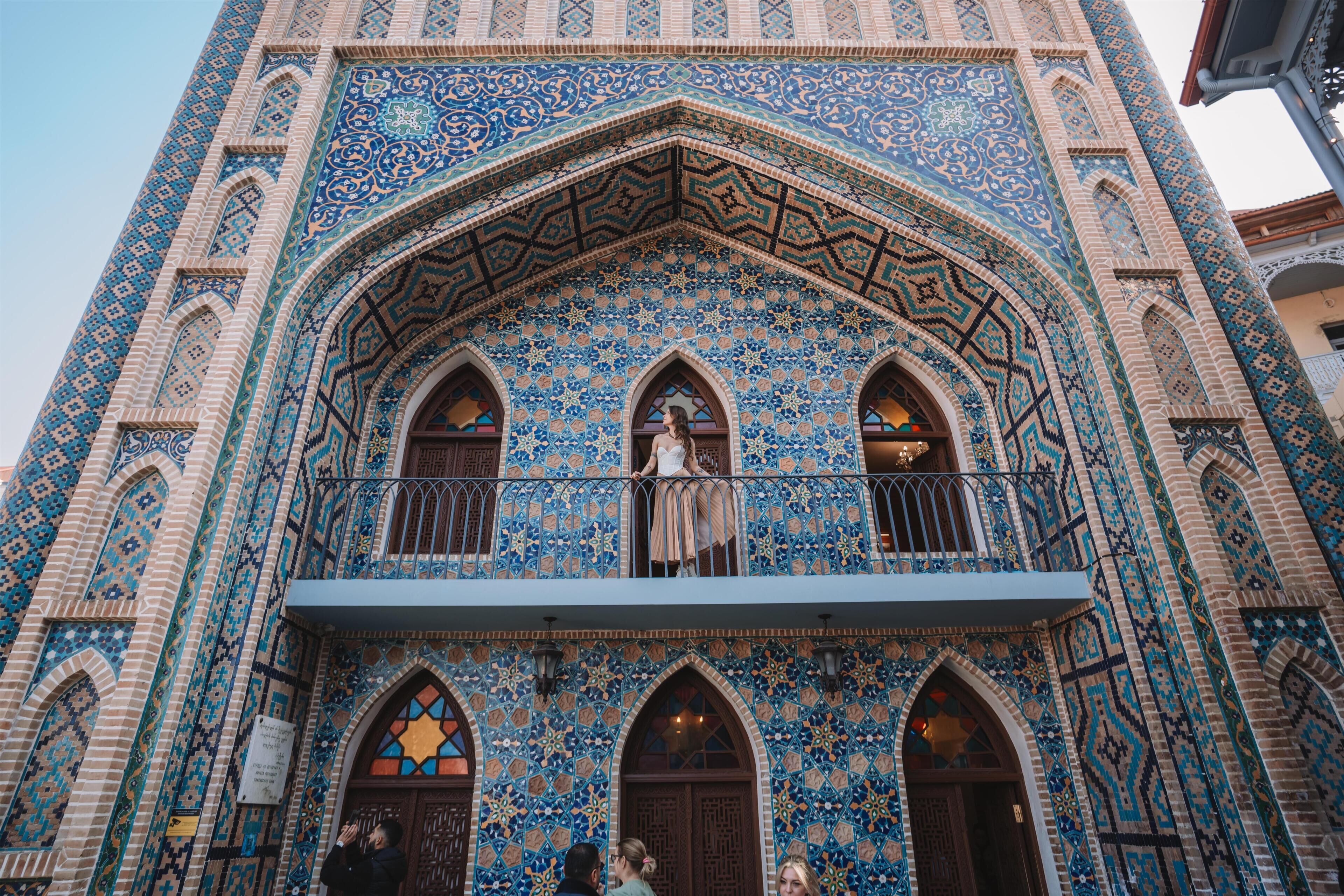 A building with intricate blue and beige tile patterns, arched windows, and a balcony with a railing.