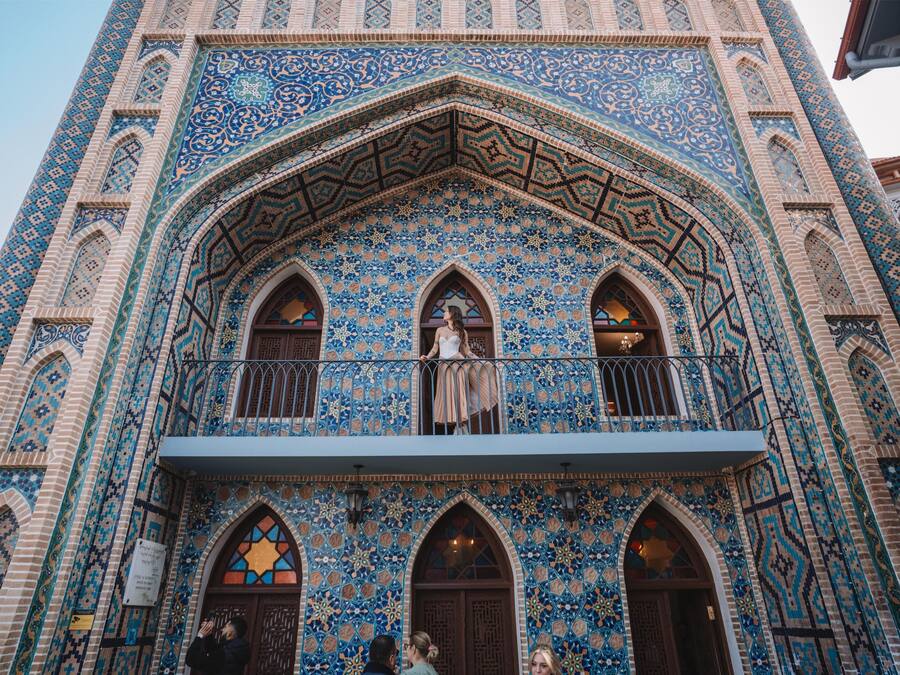 A building with intricate blue and beige tile patterns, arched windows, and a balcony with a railing.