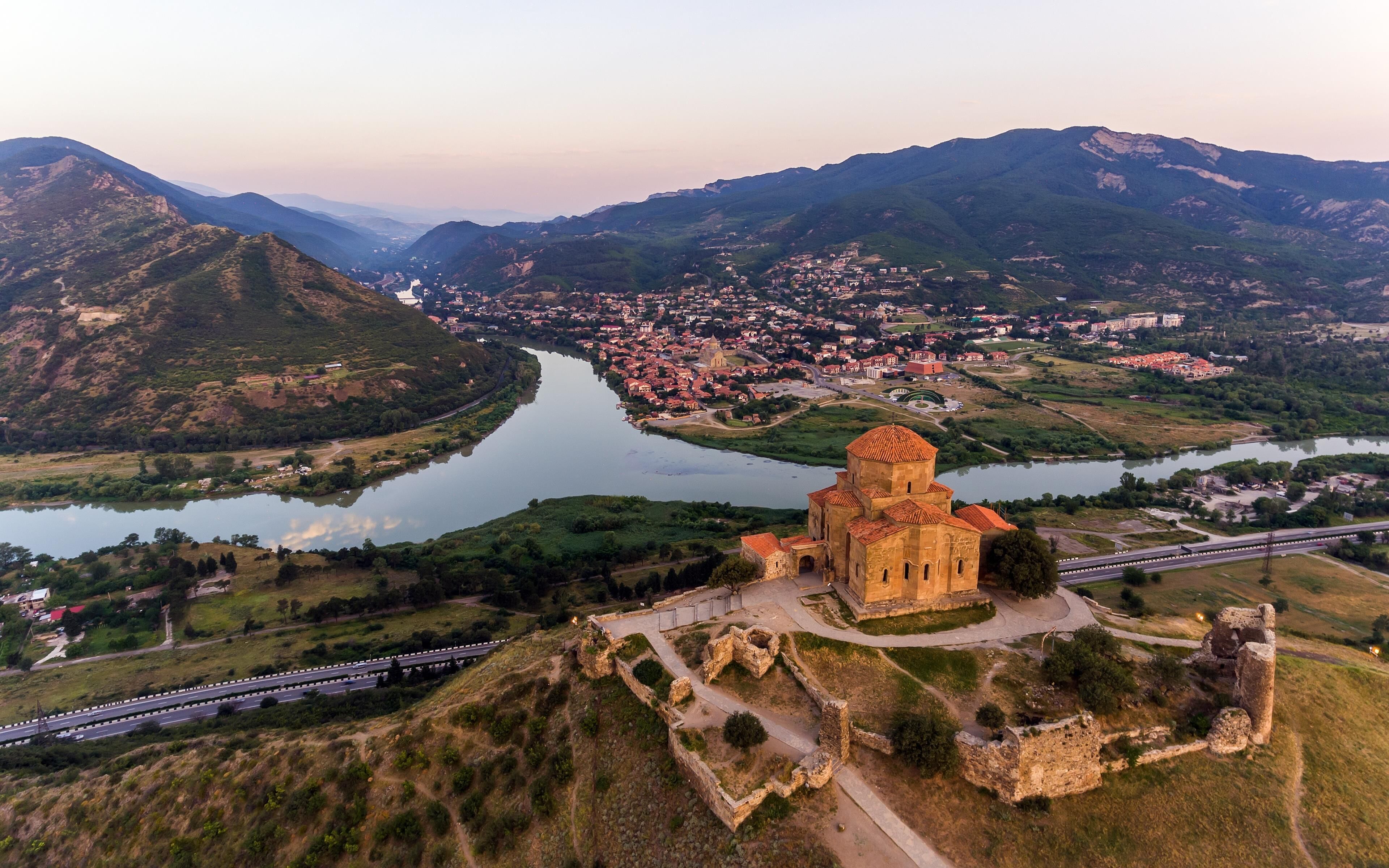 A historical building with a dome, surrounded by a river and mountains, with a highway nearby.