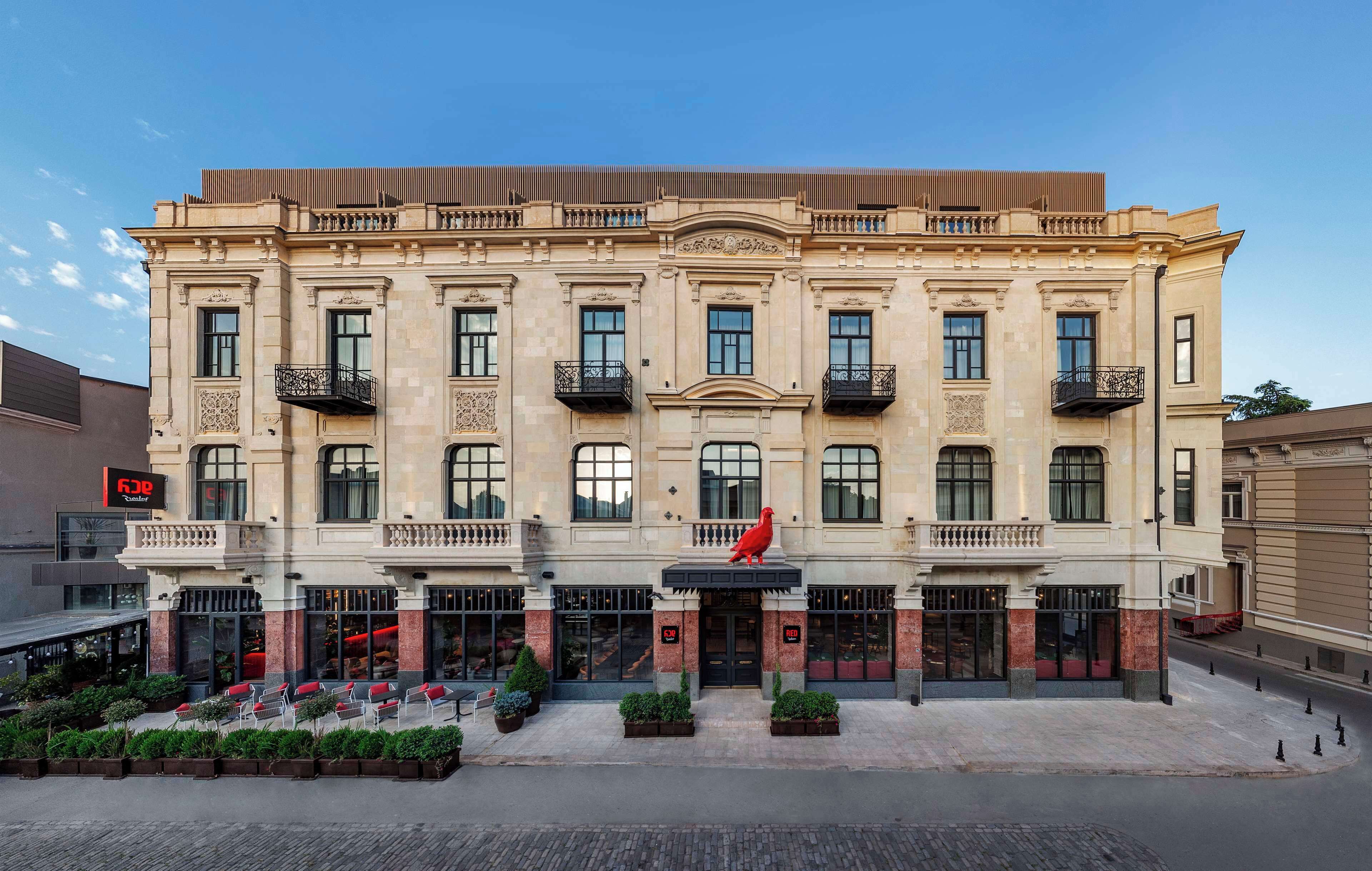 Un edificio histórico con una entrada central, ventanas grandes y una escultura de un pájaro rojo en la fachada.