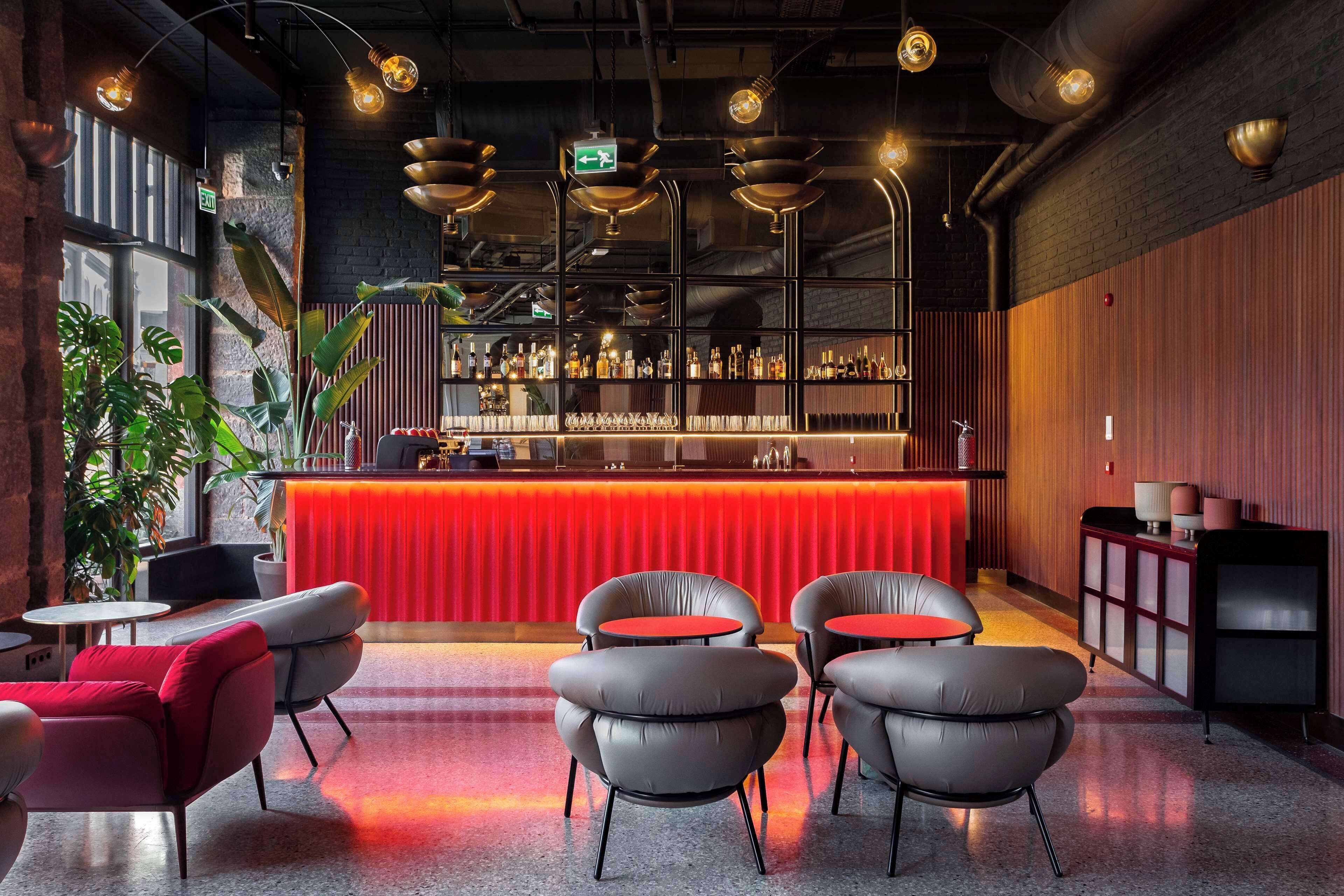 A modern bar area with a red counter, multiple seating options, and a variety of bottles on shelves.