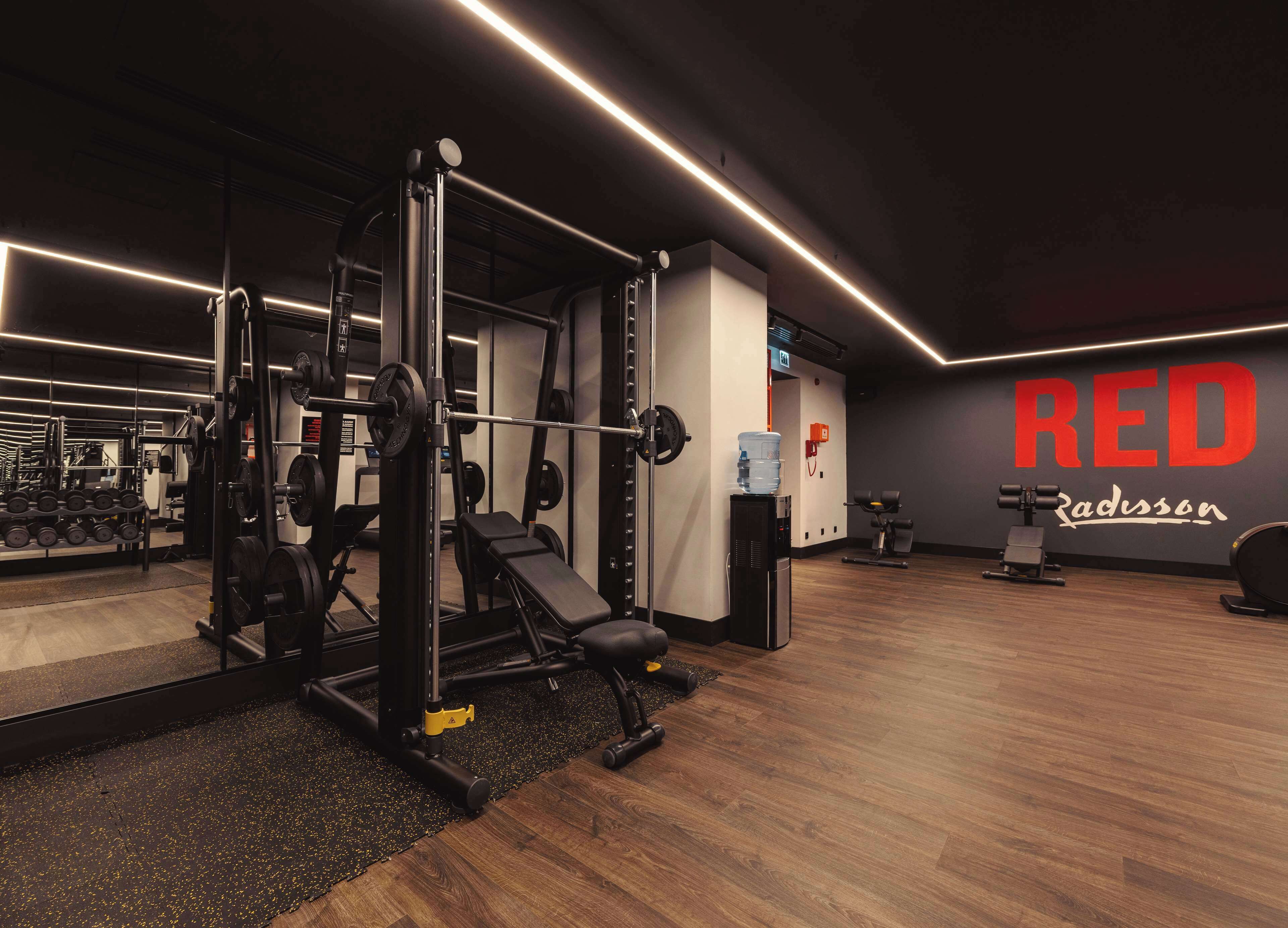 A gym with weightlifting equipment, a water dispenser, and a wall with the text "RED Radisson".