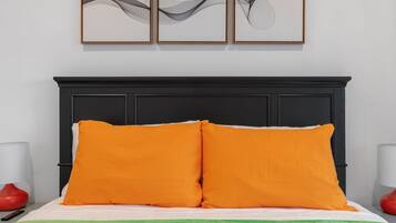 A bed with two orange pillows, a black headboard, and a green blanket. There are two red lamps on either side of the bed.