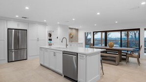 Une cuisine moderne avec des meubles blancs, des appareils en acier inoxydable et un grand îlot central doté d’un lave-vaisselle.
