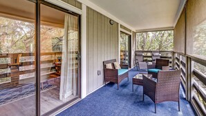A covered balcony with wicker furniture, a glass door leading to a room with a patterned rug, and a view of trees. - 3e Amelia Landings 2 Bedroom Condo by RedAwning (Fernandina Beach)