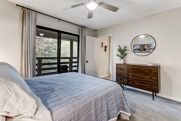 Un dormitorio con cama, cómoda, ventilador de techo y una ventana grande con cortinas.