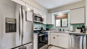 A modern kitchen with stainless steel appliances, white cabinetry, and a window with blinds. - 3e Amelia Landings 2 Bedroom Condo by RedAwning (Fernandina Beach)