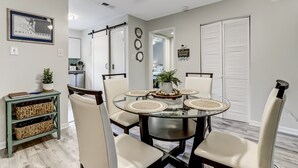 A dining area with a round glass table, beige chairs, and a potted plant. - 3e Amelia Landings 2 Bedroom Condo by RedAwning (Fernandina Beach)