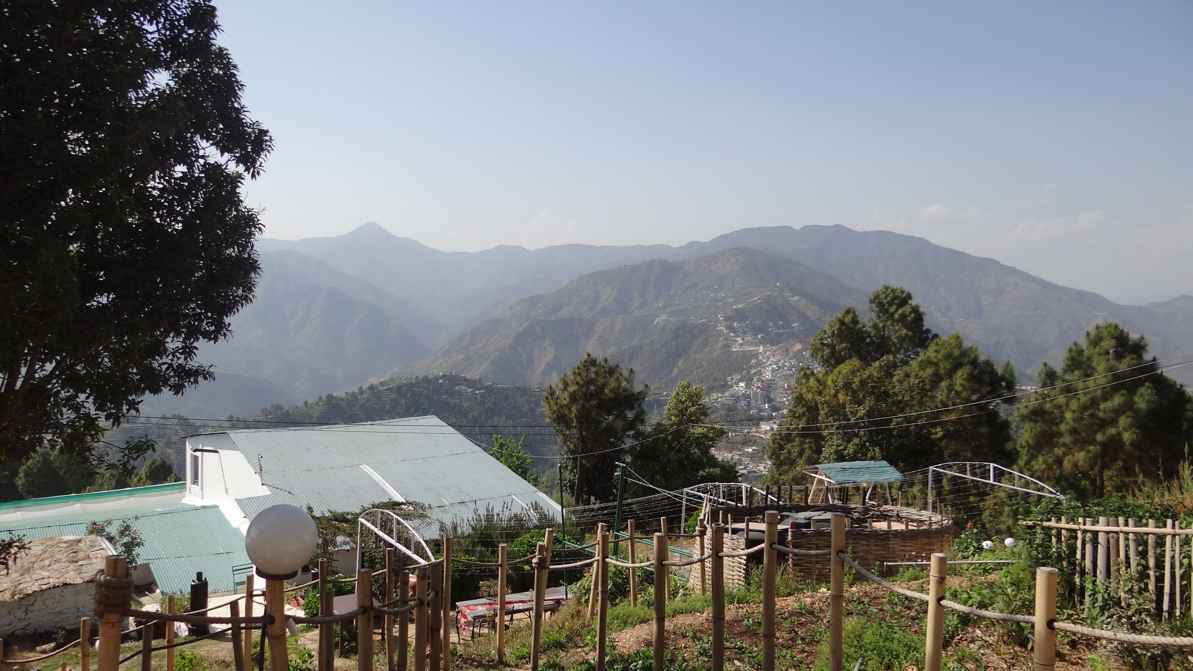 Vista de un paisaje montañoso con un edificio que tiene techo verde y una zona de juegos con estructuras de madera y barreras de cuerda.
