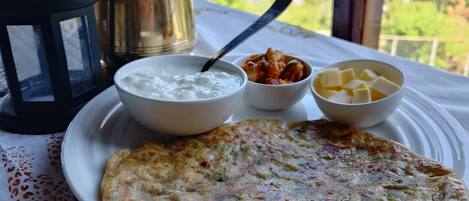 A table with a flatbread, a bowl of yogurt, and a bowl of butter, set on a tablecloth near a window with a view of greenery.