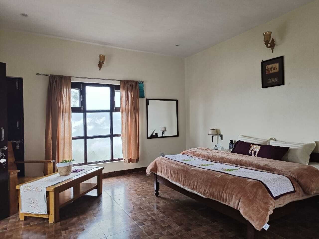 Un dormitorio con una cama grande, un banco de madera, una ventana con cortinas, una lámpara de pared y un cuadro enmarcado.