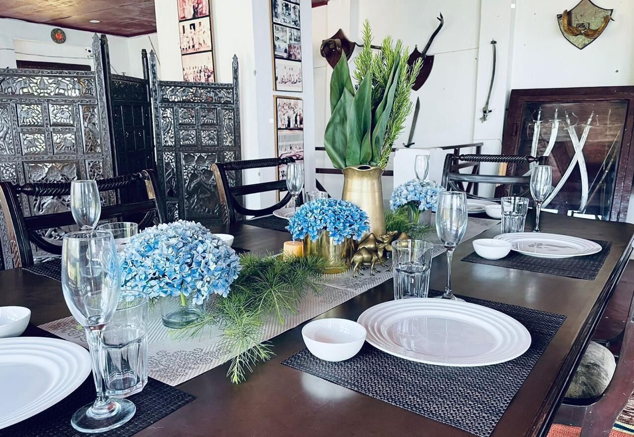 Une table à manger dressée avec des assiettes, des verres et un centre de table composé de fleurs bleues et de verdure.