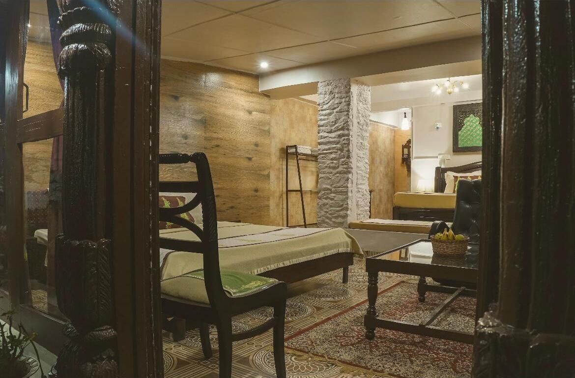 Una habitación con cama, una silla, una mesita y un pilar de piedra.